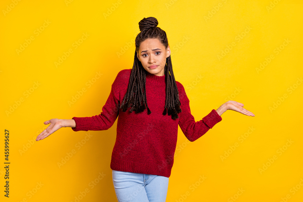 Photo of sweet upset dark skin lady wear red pullover shrugging shoulders isolated yellow color background Photo of sweet upset dark skin lady wear red pullover shrugging shoulders isolated yellow color background