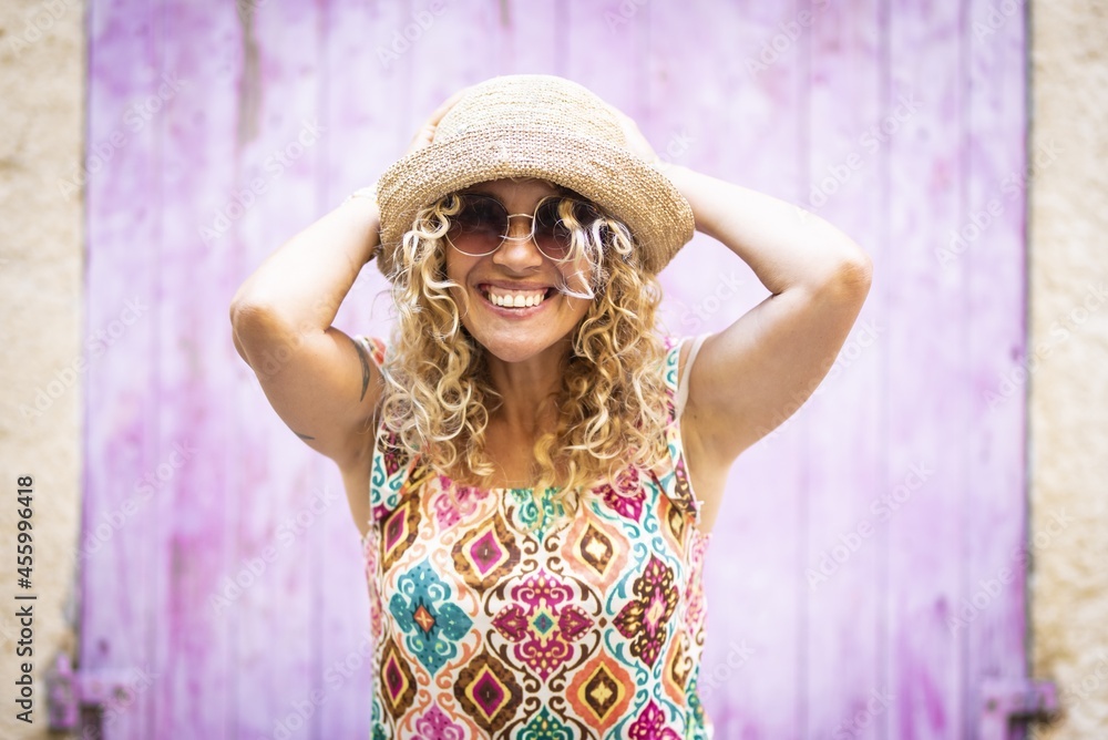 Portrait of beautiful enthusiastic young woman in sunglasses and straw hat posing outdoors with her head in hands. Portrait of excited hipster woman with hands behind her straw hat
