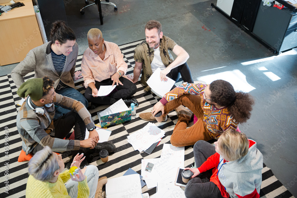 Team sitting on office floor, discussing paperwork Team sitting on office floor, discussing paperwork