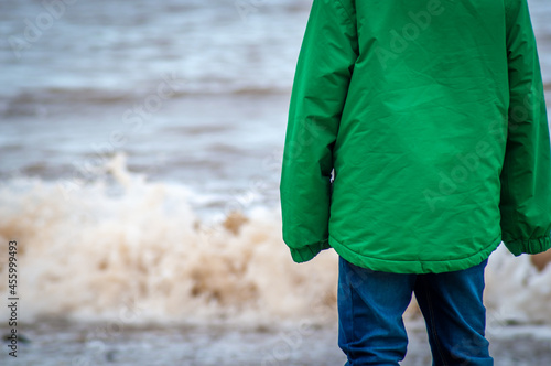 Photography Closeup of the middle of a child looking out to sea just as a wave is at the sho