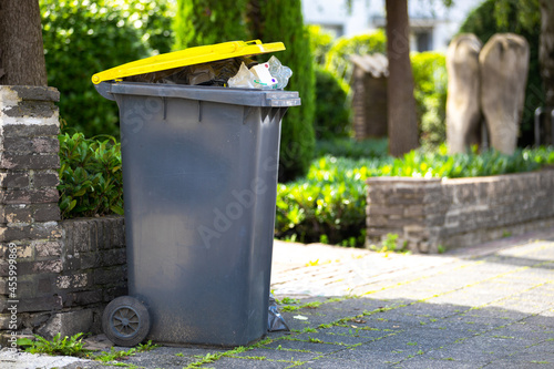 full garbage trash can standing at sidewalk next to street waiting to get collected and empty the recyclable plastic dump out of the black yellow container