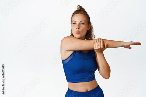 Young sport woman control breathing, stretching her arm. Fitness girl warm up, doing worout for healthy body, standing in activewear against white background