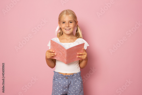 Beautiful girl with bond hair holds a notebook and smiles, picture isolated on pink background