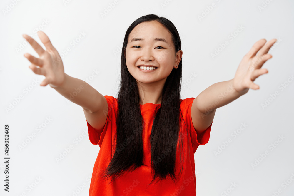 Portrait of asian girl spread hands for hug, smiling and looking happy, standing in red t-shirt against white background Portrait of asian girl spread hands for hug, smiling and looking happy, standing in red t-shirt against white background