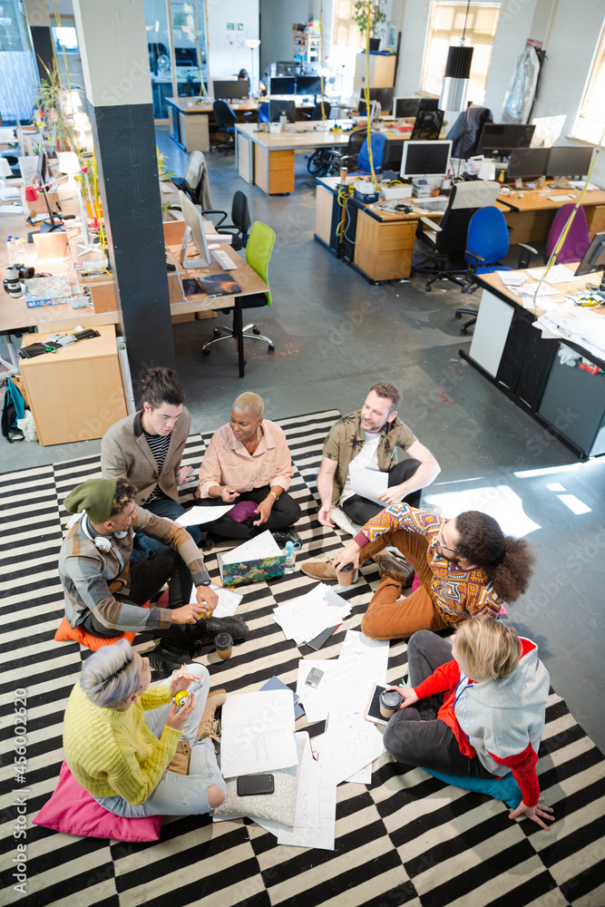 Team sitting on office floor, discussing paperwork Team sitting on office floor, discussing paperwork