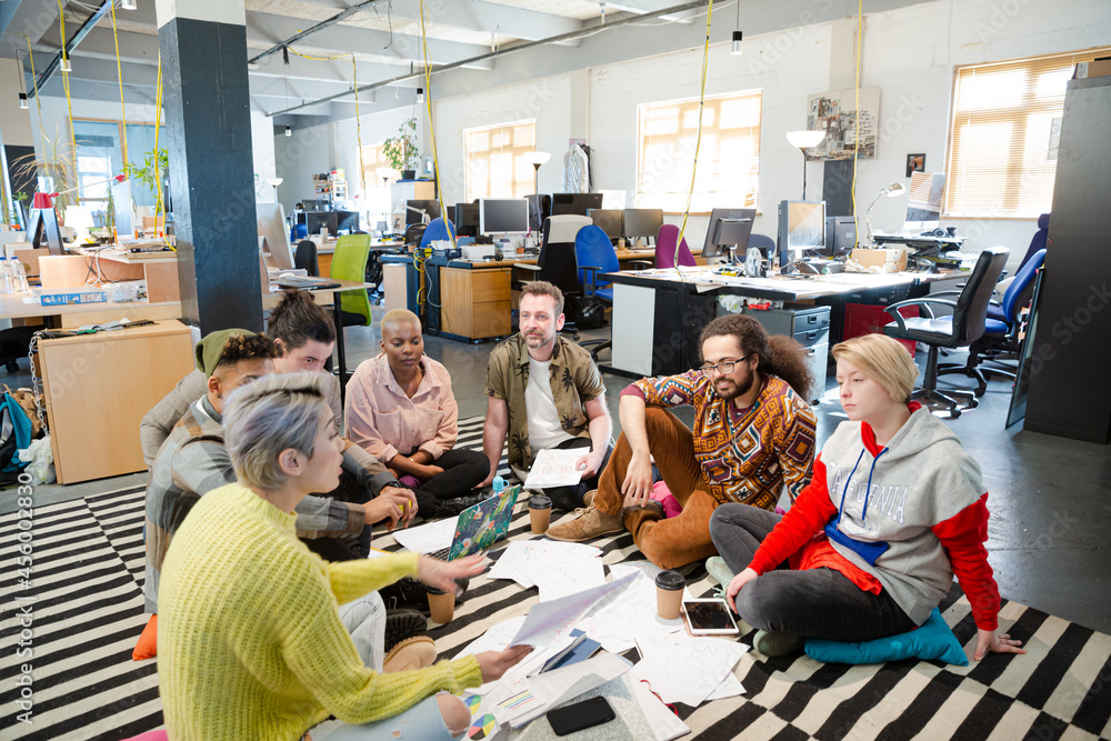 Team sitting on office floor, discussing paperwork Team sitting on office floor, discussing paperwork