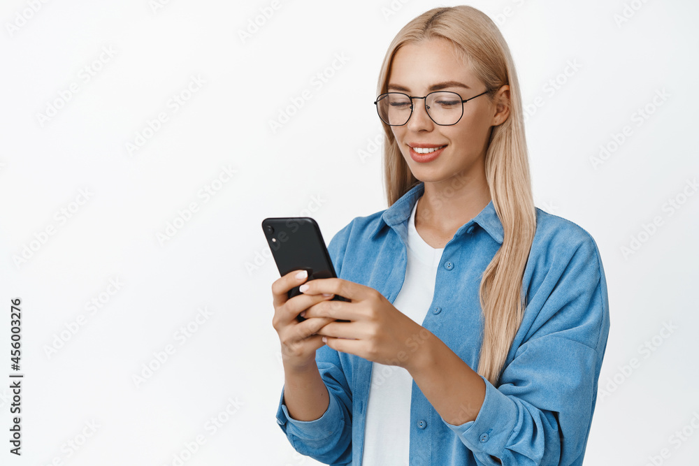 Cellular. Young woman using app on mobile phone, reading smartphone with glasses, standing over white background Cellular. Young woman using app on mobile phone, reading smartphone with glasses, standing over white background