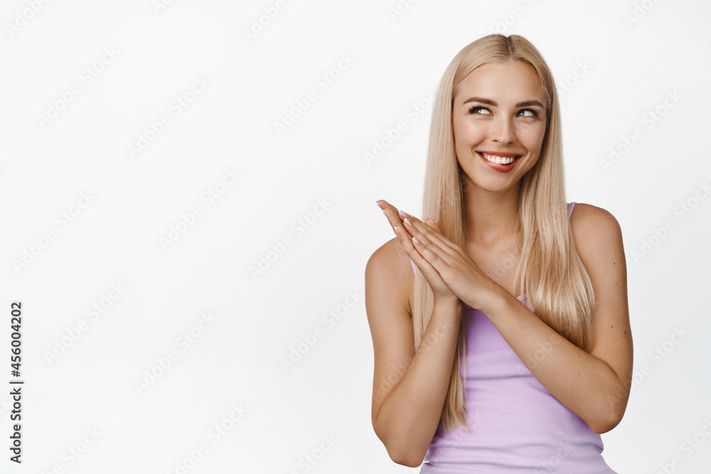 Image of coy blond girl smiling, rubbing hands and looking cunning, thinking of something, evil genius face, standing over white background Image of coy blond girl smiling, rubbing hands and looking cunning, thinking of something, evil genius face, standing over white background