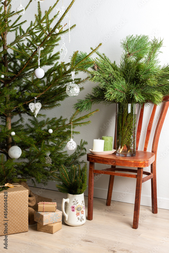 Christmas tree with white toys, old chair with a vase with pine branches, gift boxes under the tree, part of home interior Christmas tree with white toys, old chair with a vase with pine branches, gift boxes under the tree, part of home interior