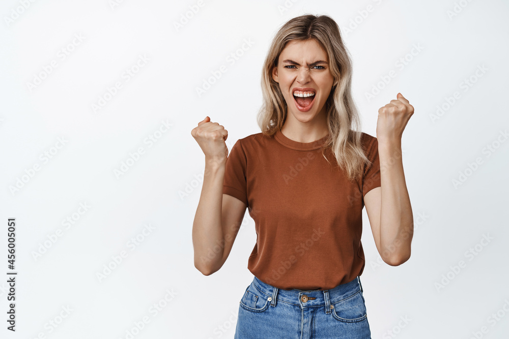 Cheerful blond woman clench fists and shouting to boost confidence, encourage herself, standing against white background Cheerful blond woman clench fists and shouting to boost confidence, encourage herself, standing against white background