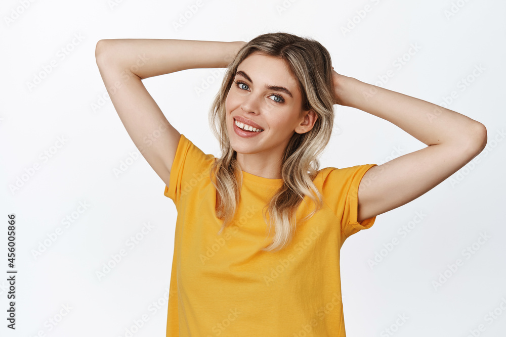 Image of happy beautiful girl relaxing, resting with hands behind head and smiling, looking free and careless, standing against white background Image of happy beautiful girl relaxing, resting with hands behind head and smiling, looking free and careless, standing against white background