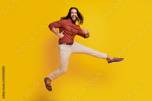 Portrait of funky positive guy jump raise thumb up open mouth on yellow background