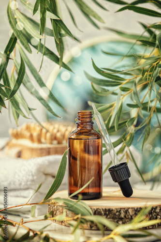 Amber serum cosmetic bottle on wooden geometric pedestal podium, wooden massage brush, eucalyptus leaves, mirror and towels. Eco friendly massage, anti aging serum with peptides, cosmetics, skincare photo