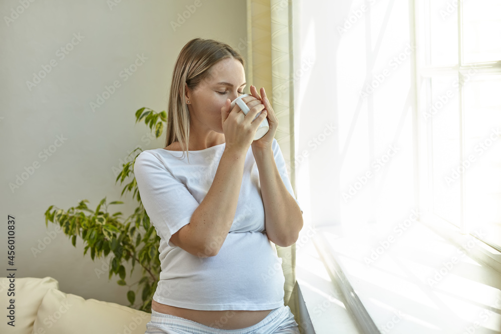 Woman in standing by the window and drinking coffee Woman in standing by the window and drinking coffee