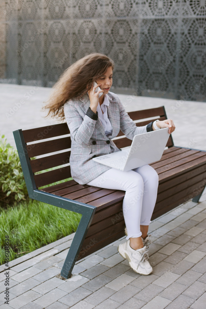 Woman working on laptop sitting on abench near modern office building Woman working on laptop sitting on abench near modern office building