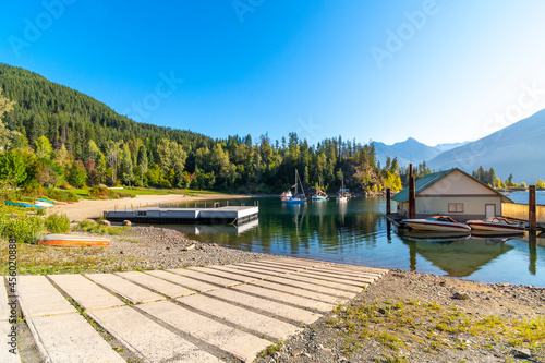 Morning sunlight at Kaslo Bay on Kootenay Lake in the small rural town of Kaslo, BC Canada, with a boat launch ramp and boathouses in the water.