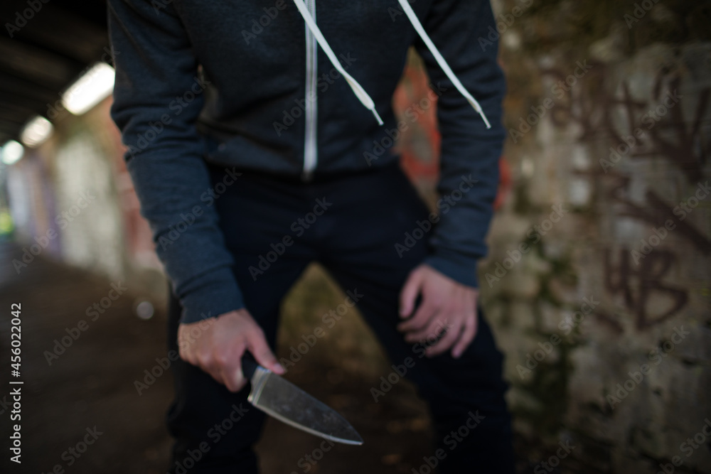 Dangerous man in hoody holding knife weapon in urban tunnel Dangerous man in hoody holding knife weapon in urban tunnel