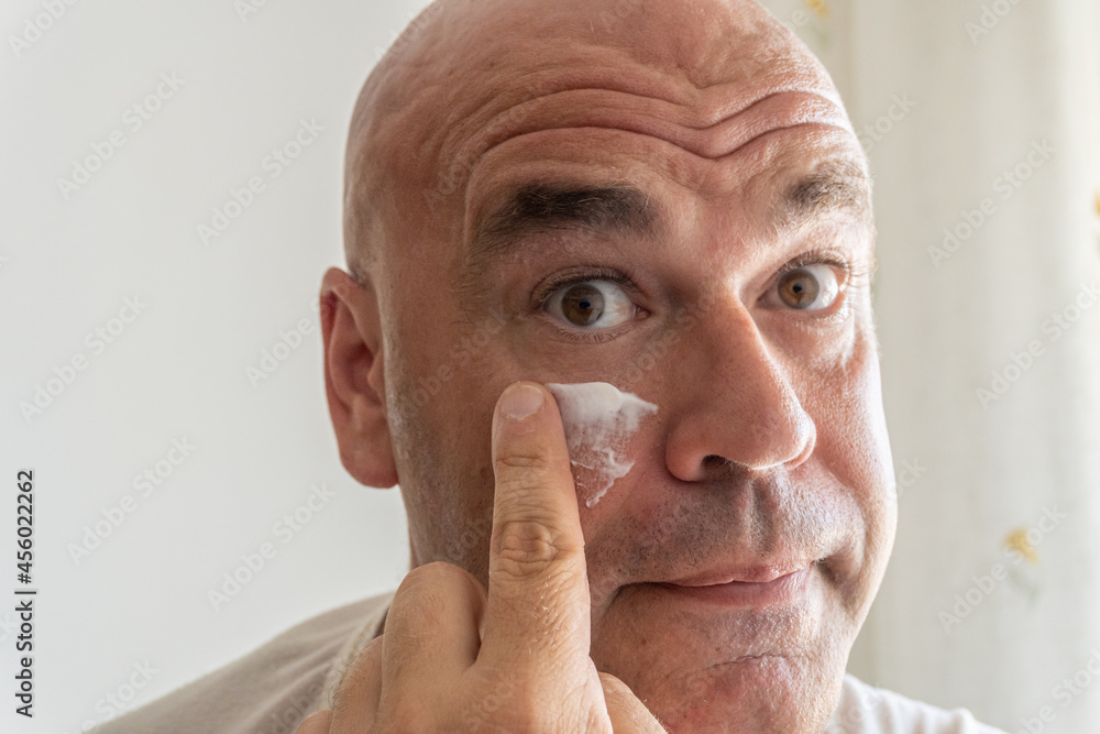 Close-up of a middle-aged Caucasian man applying facial cream to his face. 