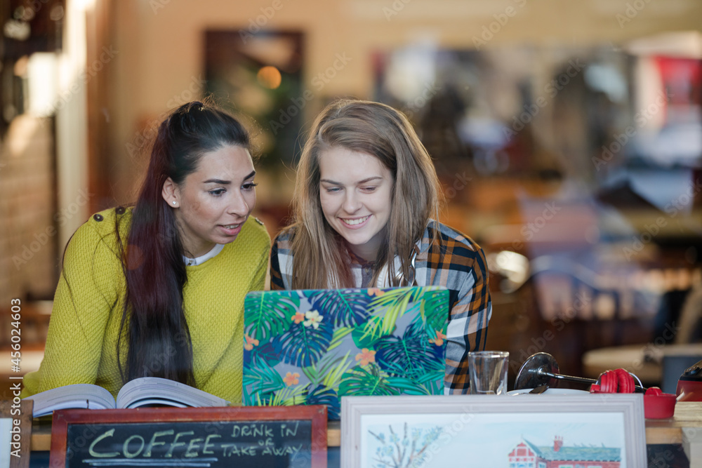 Young female college students studying at laptop in cafe window Young female college students studying at laptop in cafe window