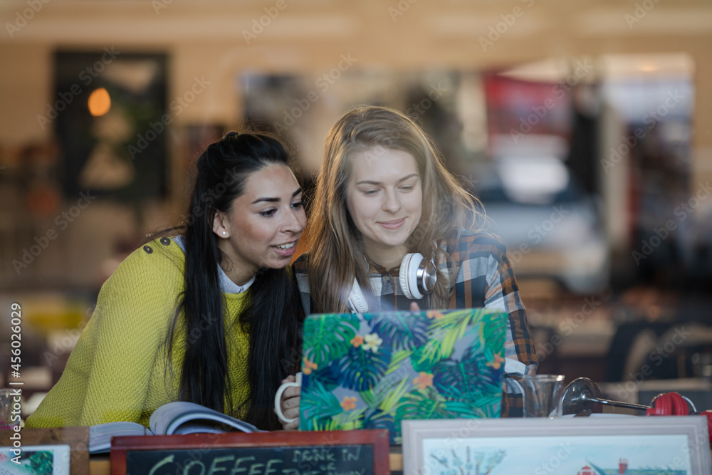 Fototapeta premium Young female college students studying at laptop in cafe window