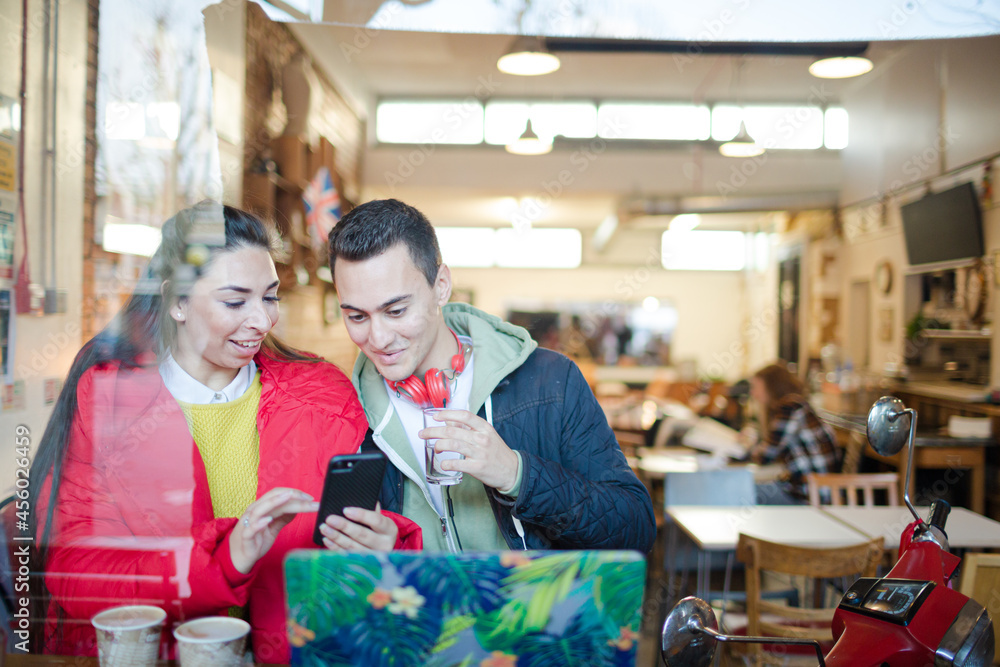 Young couple using smart phone and laptop in cafe