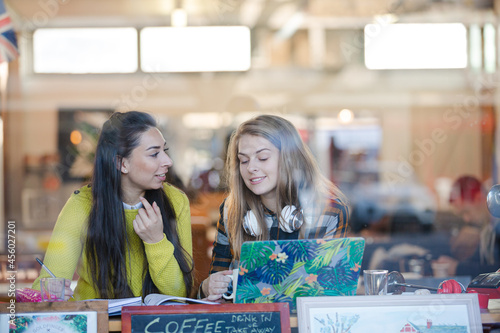 Young female college students studying at laptop in cafe window