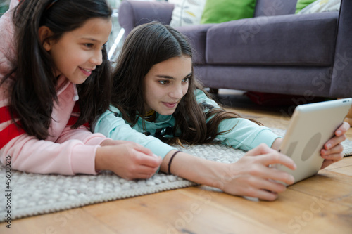 Sisters using digital tablet on living room floor