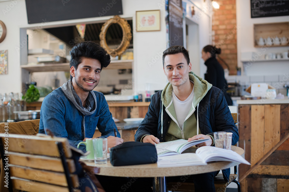 Portrait confident young male college students studying at cafe table