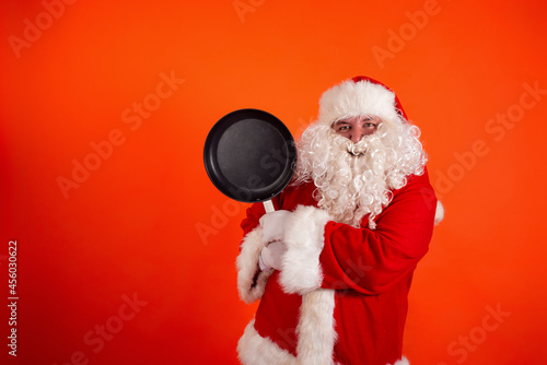 Funny fat Sanat Claus with a frying pan in his hands on an orange background. Copy space.