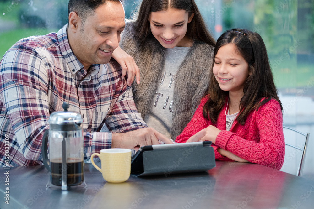 Father and daughters using digital tablet in morning kitchen Father and daughters using digital tablet in morning kitchen