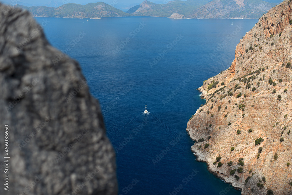 Sailing boat sails into the open sea from a rocky gorge of Butterfly Valley, Turkey