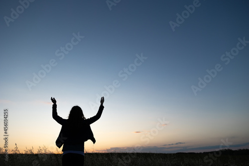 silhouette of a person in sunset in field with hands raised in praise
