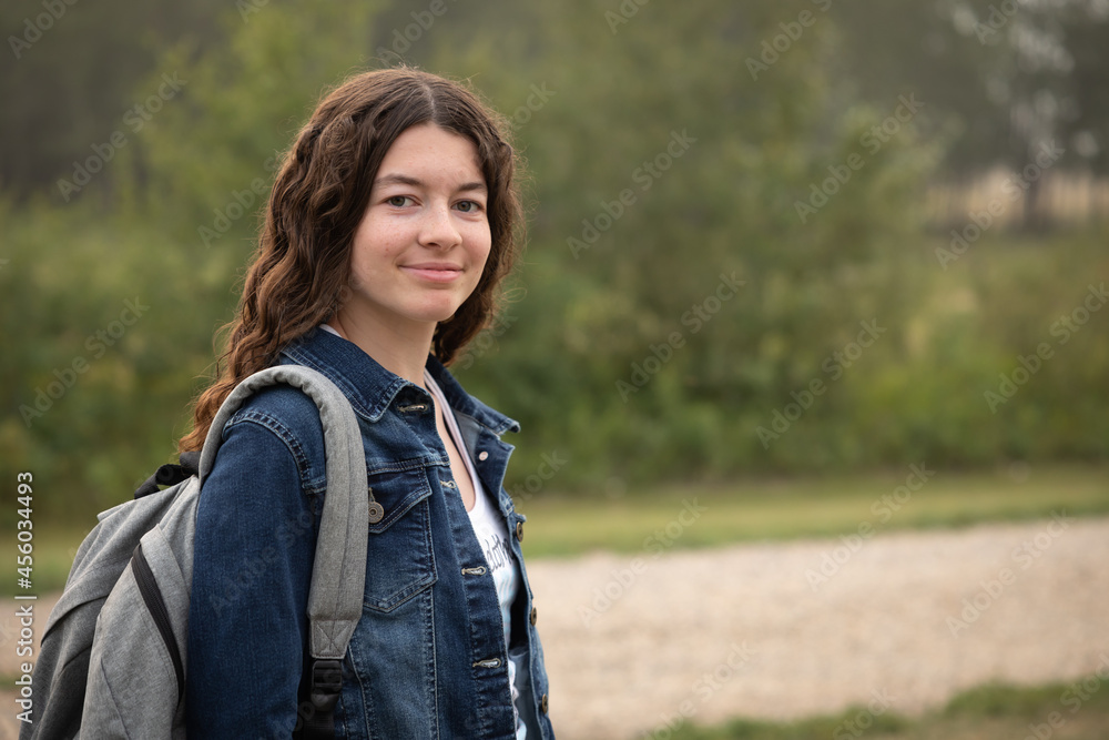 portrait of a teen girl smiling wearing backpack and denim jacket outdoors with copy space