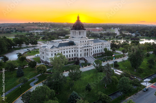 South Dakota State Capitol building in Pierre, SD. Aerial drone view at sunrise with golden glow behind domed roof.