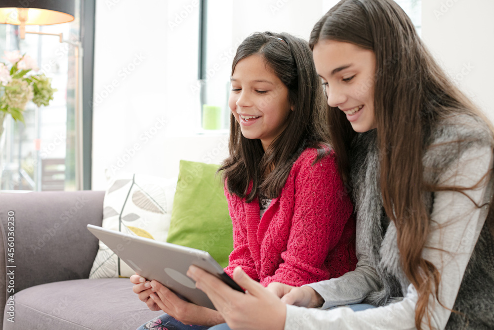 Happy sisters using digital tablet on living room sofa Happy sisters using digital tablet on living room sofa