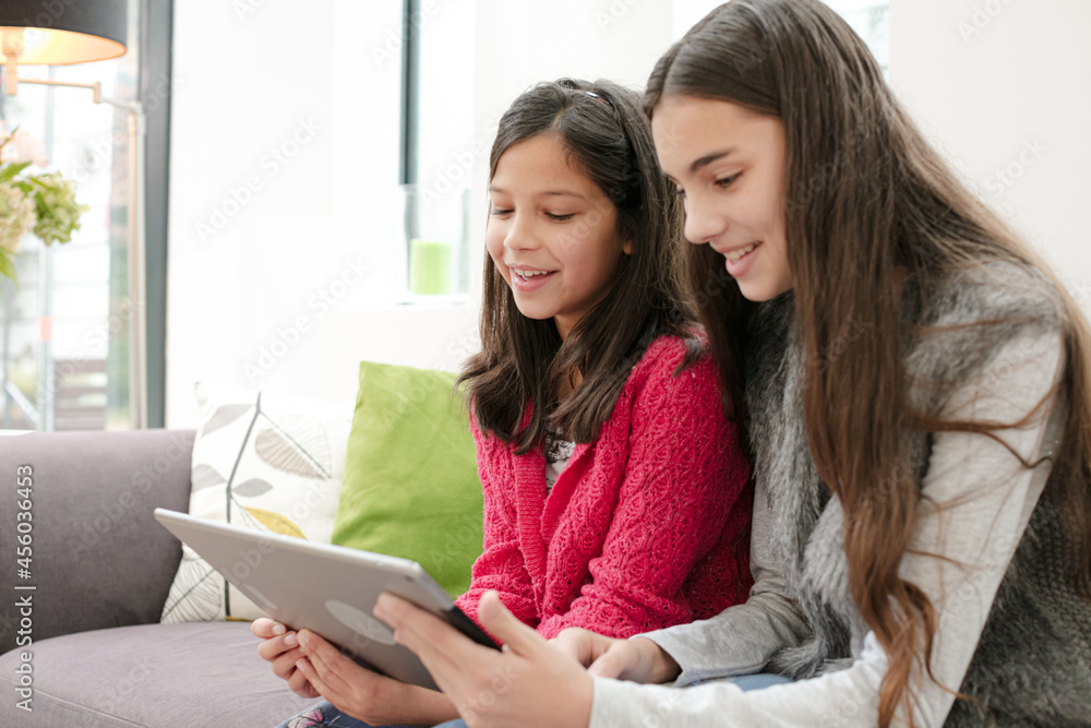 Happy sisters using digital tablet on living room sofa Happy sisters using digital tablet on living room sofa