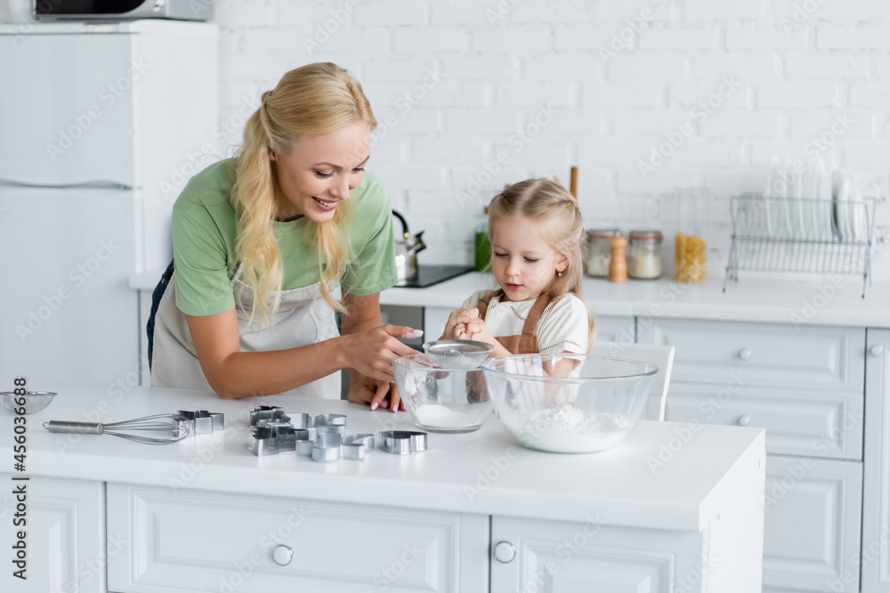 girl sifting flour with sieve into bowl near happy mother girl sifting flour with sieve into bowl near happy mother