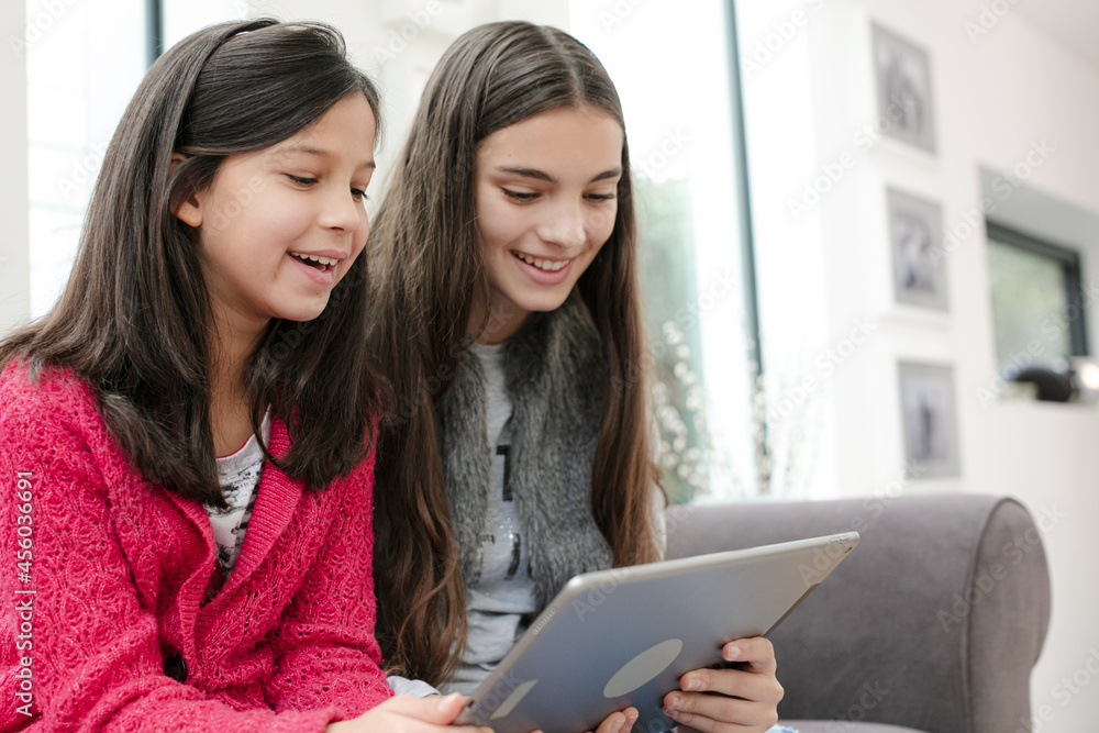 Happy sisters using digital tablet on living room sofa Happy sisters using digital tablet on living room sofa