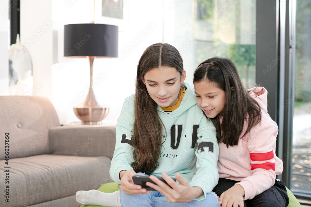 Playful sisters taking selfie with smart phone in living room Playful sisters taking selfie with smart phone in living room