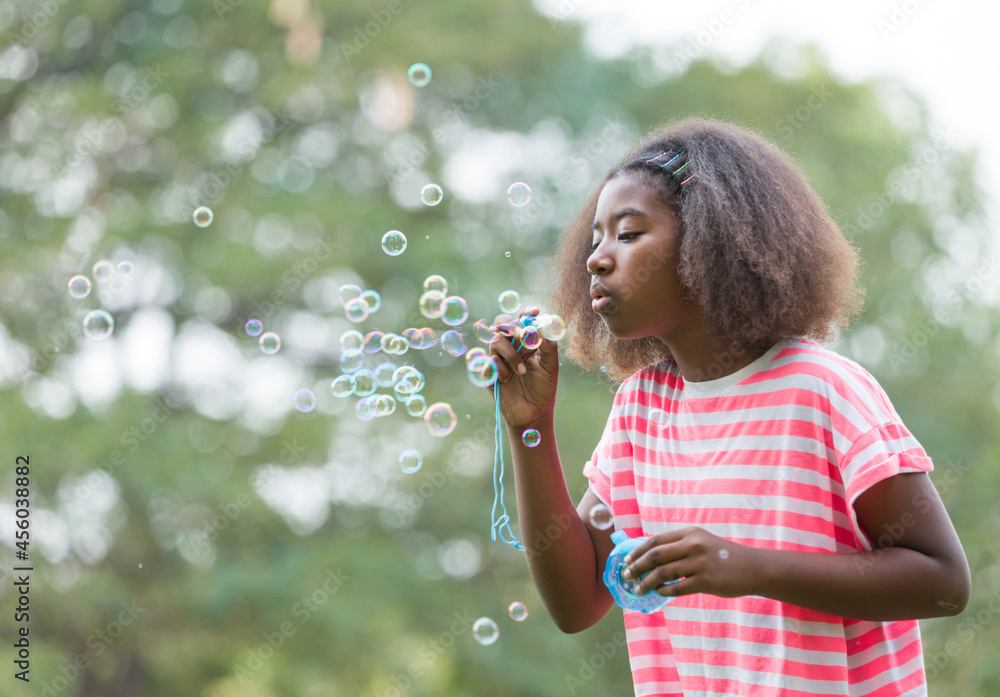 Little African American girl blowing soap bubbles in the park.