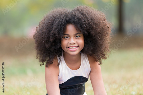 Portrait of happy smiling African American little girl doing yoga outdoor. Little afro girl with curly hairstyle practicing yoga in the park.