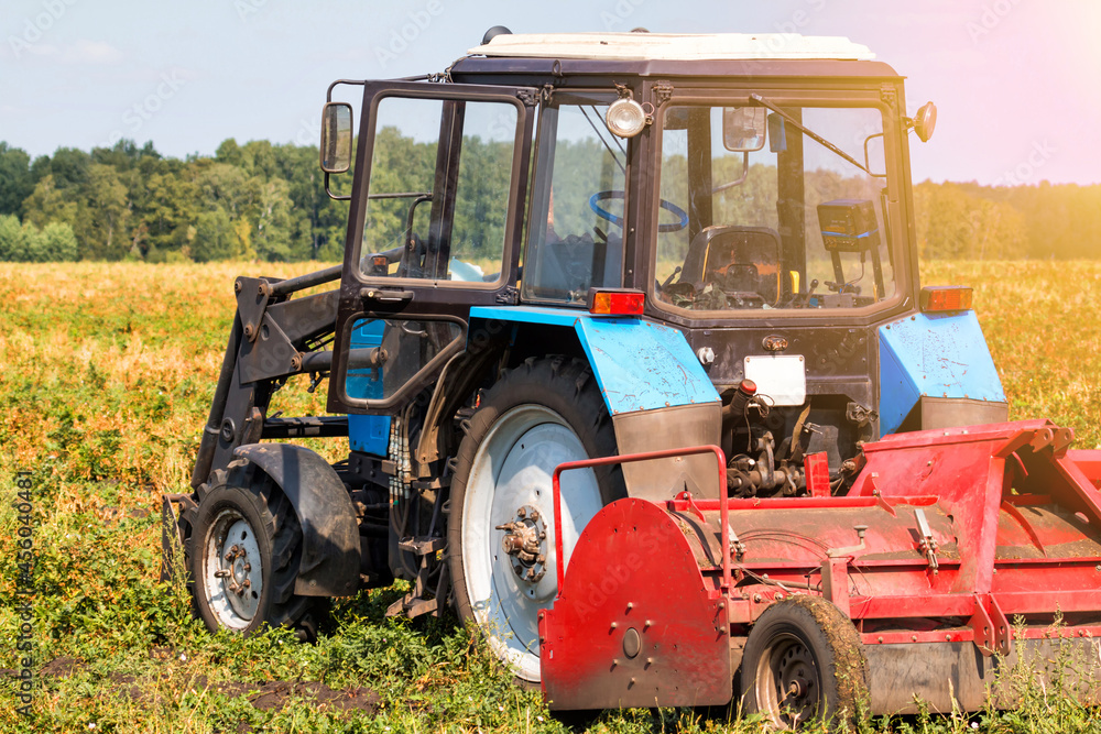 Fototapeta premium Modern wheeled agricultural tractor with harvesting equipment on an field