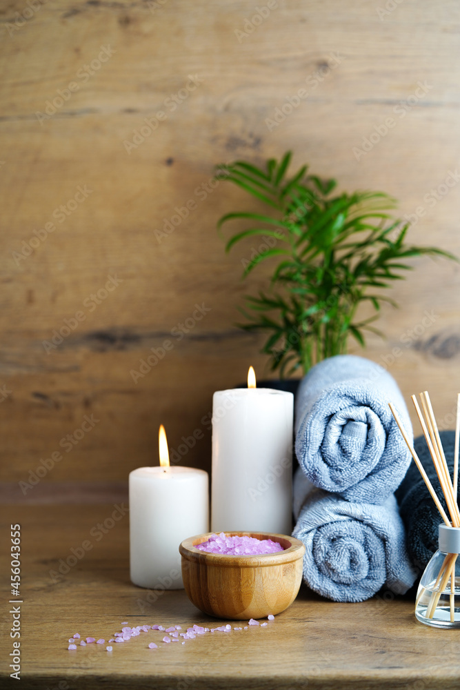 spa and aromatherapy concept-candles, towels, pink sea salt and an aromatic reed diffuser on a wooden table.