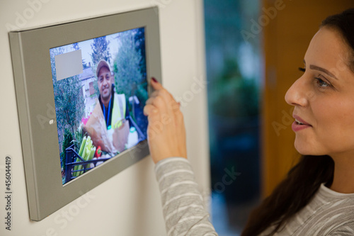Smiling woman watching deliveryman approaching front door from smart home automation screen
