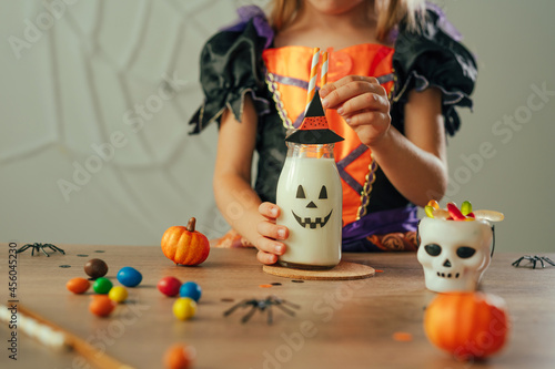 Close up of little girl dressed Halloween witch costume sitting at the table with milkshake