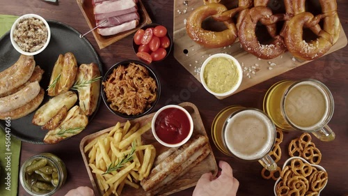 Traditional German Cuisine. Putting tray with smoked sasuages and fried potatoes top view, pickled cucumbers, bratwursts and fresh pretzels, beer on table. Composition of Cooked National Czech Food.  photo