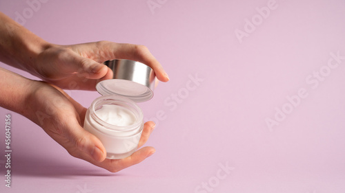 Cream jar in hand isolated on purple background. Woman holding jar with cosmetic cream