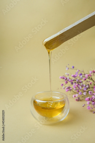 Depilation and beauty concept - sugar paste or wax, honey for hair removal drips from wooden wax sticks in a jar on a floral background
