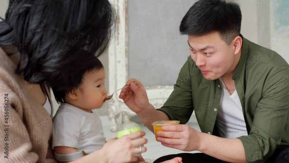 Handsome Young Father Feed Little Baby With Fruit or Vegetable Mash Food. Child Eating. Good Appetite. Happy Asian Family Relationship With Lovely Child. Father and Mother Young Parents With Baby Kid. Handsome Young Father Feed Little Baby With Fruit or Vegetable Mash Food. Child Eating. Good Appetite. Happy Asian Family Relationship With Lovely Child. Father and Mother Young Parents With Baby Kid.