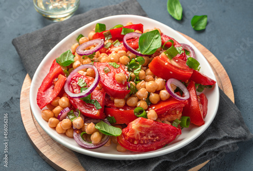 Healthy salad with chickpeas, tomatoes and fresh herbs on a gray-blue background in a white plate.
